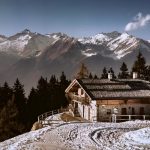 maison dans les hauteurs d'une montagne. On voit de la neige, des sapins et des montagnes au loin.