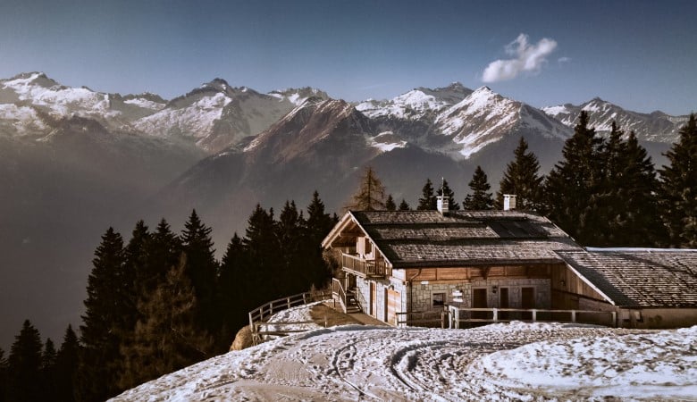 maison dans les hauteurs d'une montagne. On voit de la neige, des sapins et des montagnes au loin.