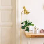 stylish and elegant home interior with wooden desk, grey velvet chair, design accessories, gold lamp and hanging mirror on the white wall. piece of design woman's room. white wooden door. copy space.