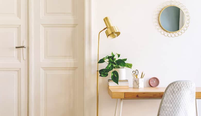 stylish and elegant home interior with wooden desk, grey velvet chair, design accessories, gold lamp and hanging mirror on the white wall. piece of design woman's room. white wooden door. copy space.