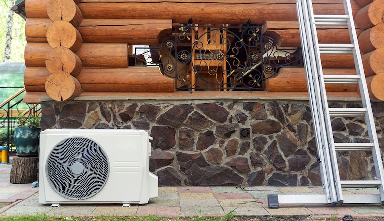 new modern hvac air conditioning external compressor unit preapred for installation or replacement near wall of wooden log residential country cottage. ladder and equipment for service and maintenance