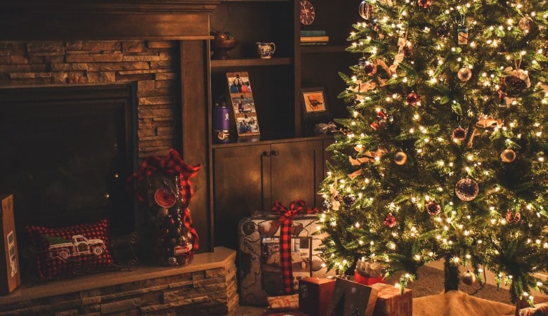 Sapin vert décoré d'une guirlande et de boules de Noël. Au pied du sapin, il y a des cadeaux.