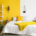 Chambre avec un lit deux places. Le mur est peint en jaune à gauche et blanc à droite.