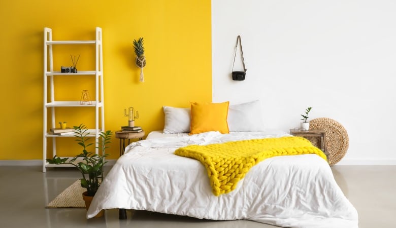 Chambre avec un lit deux places. Le mur est peint en jaune à gauche et blanc à droite.