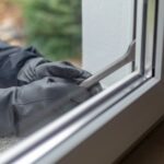 Personne avec des gants et une clé à molette essayant de s'introduire dans un logement en passant par la fenêtre