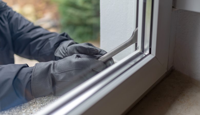 Personne avec des gants et une clé à molette essayant de s'introduire dans un logement en passant par la fenêtre