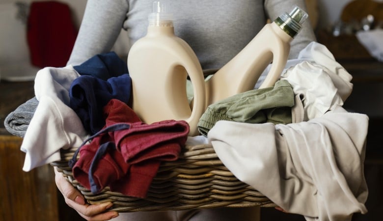 personne tenant une corbeille en bois rempli de vêtement et de linge avec deux bidons de lessive