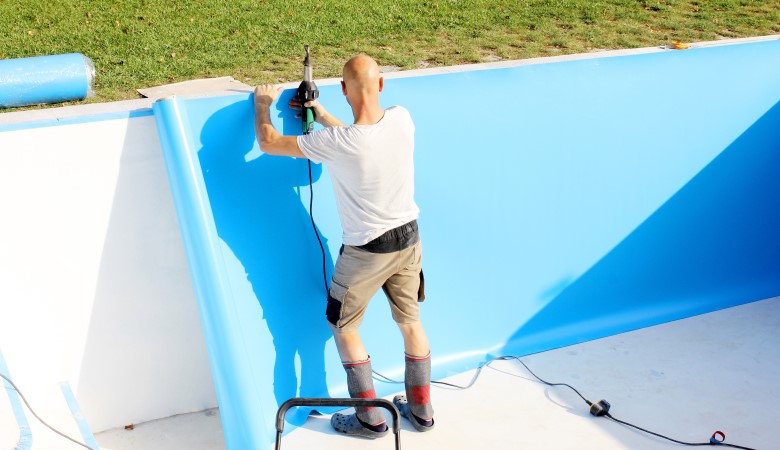 Un travailleur pose un revêtement sur les parois d'une piscine creusée.