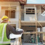 travailleur qui regarde un plan devant une maison en construction