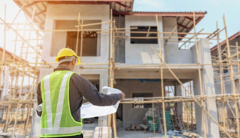 travailleur qui regarde un plan devant une maison en construction