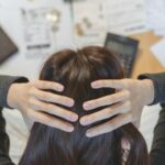 Une femme se tient la tête entre ses deux mains face à des factures et une calculatrice.