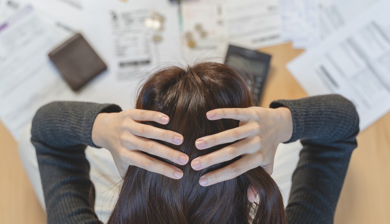 Une femme se tient la tête entre ses deux mains face à des factures et une calculatrice.