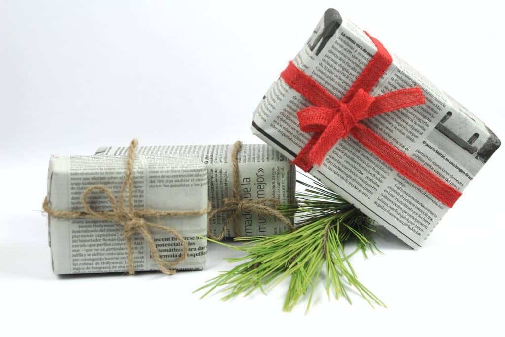 Cadeaux emballés dans du vieux papier journal avec une branche de pin, une corde et des boules vertes sur fond blanc