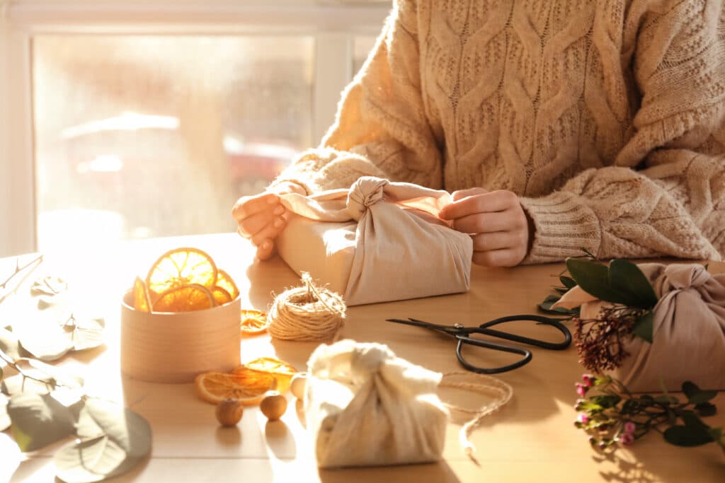 Femme emballant un paquet cadeau dans un tissu à une table