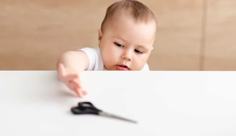 Un bébé essayant d'attraper une paire de ciseaux sur une table basse.