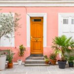 Maison colorée, avec une façade rose, et une dizaine de plante en pots devant.