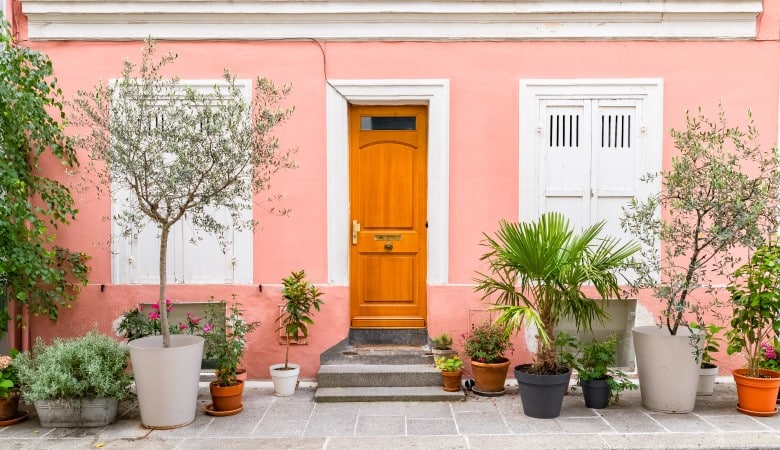 Maison colorée, avec une façade rose, et une dizaine de plante en pots devant.