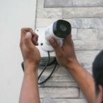 Les mains d'un monsieur (de dos) en train d'installer une caméra de surveillance