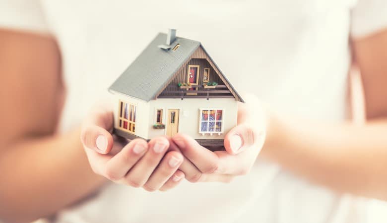 Les mains d'une jeune femme qui tiennent une maison miniature