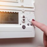 doigt d'une main de femme qui règle un thermostat accroché au mur