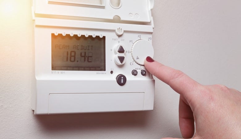 doigt d'une main de femme qui règle un thermostat accroché au mur