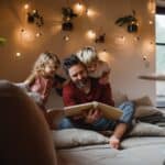 Un papa et ses deux enfants regardant un album photo sur un lit.