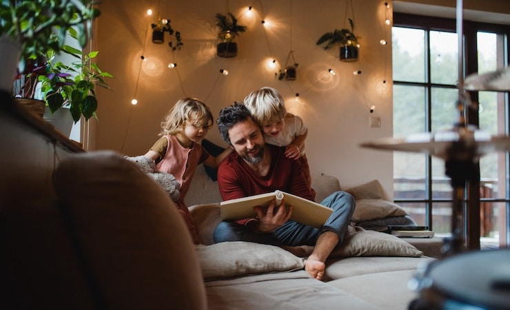 Un papa et ses deux enfants regardant un album photo sur un lit.