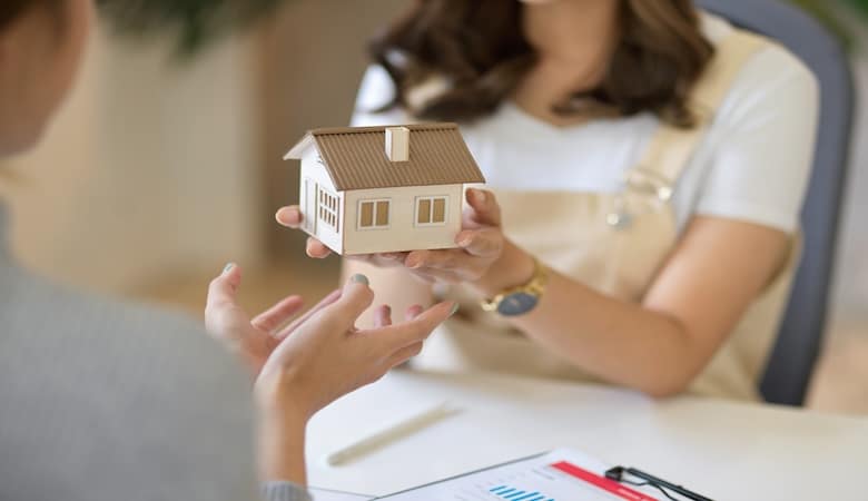 Une employée donnant à son client une petite maison fictive, représentant l'investissement d'une nouvelle maison.