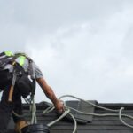 un homme qui fait des réparations sur un toit, qui est attaché par une corde