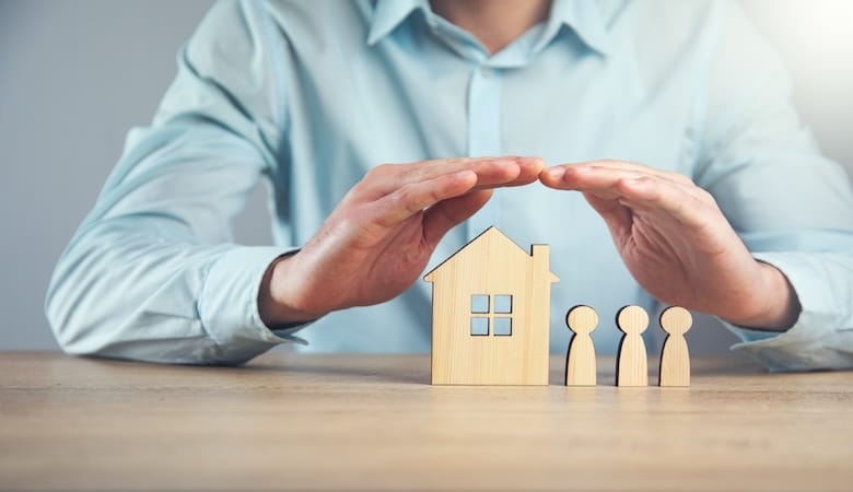 La main d'un homme protégeant une maison fictive en bois avec ses habitants.