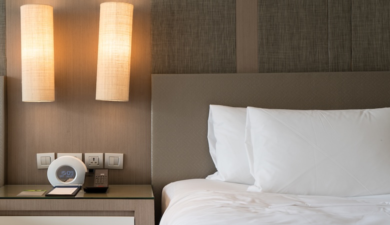 Vu sur un lit élétrique et son chevet où se trouvent une télécommande et d'autres gadgets.