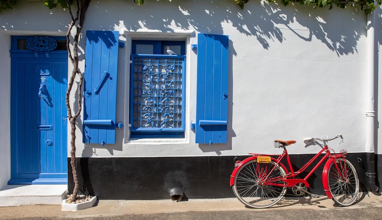 vieux vélo rouge face à une façade dans les rues d'un village de vendée, noirmoutier ou l'île de ré en france.