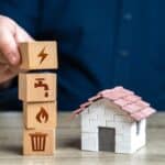 Une maison fictive avec quatre cubes en bois empilés les uns sur les autres représentants l'électricité, le feu, l'eau et une poubelle.