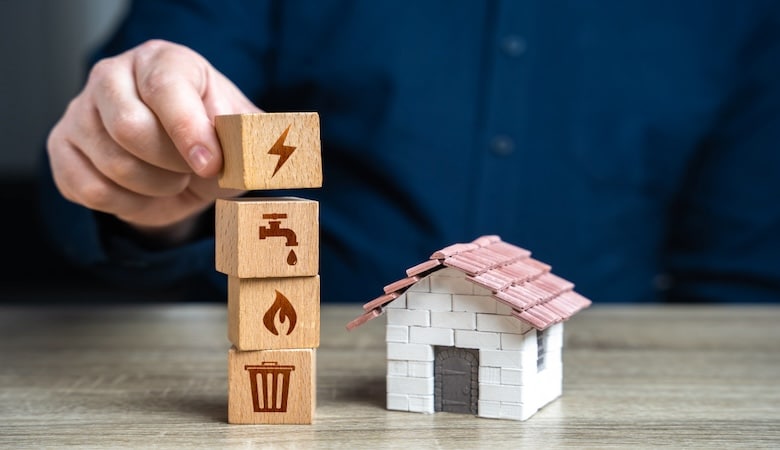 Une maison fictive avec quatre cubes en bois empilés les uns sur les autres représentants l'électricité, le feu, l'eau et une poubelle.