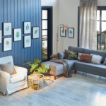 Chambre moderne bleue, canapé gris, couverture jaune et cadre en feuilles, lampe, décoration d'intérieur et parquet.