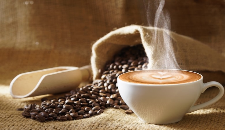 une tasse de café fumante avec un sac renversé de graine de café.