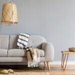 Intérieur stylé et design d'un salon avec canapé gris, table basse en bois, coussins, couvertures, lampe en rotin, panier à pantoufles et accessoires élégants. Décoration intérieure élégante.