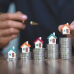 La main de la femme tient un modèle de maison mis sur la pile de pièces de monnaie avec la croissance, l'argent d'épargne pour acheter la maison et le prêt à l'investissement de l'entreprise pour le concept de l'immobilier.