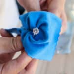 Main tenant une bague en or sertie d’un diamant, nettoyée avec un chiffon doux en microfibre bleu.