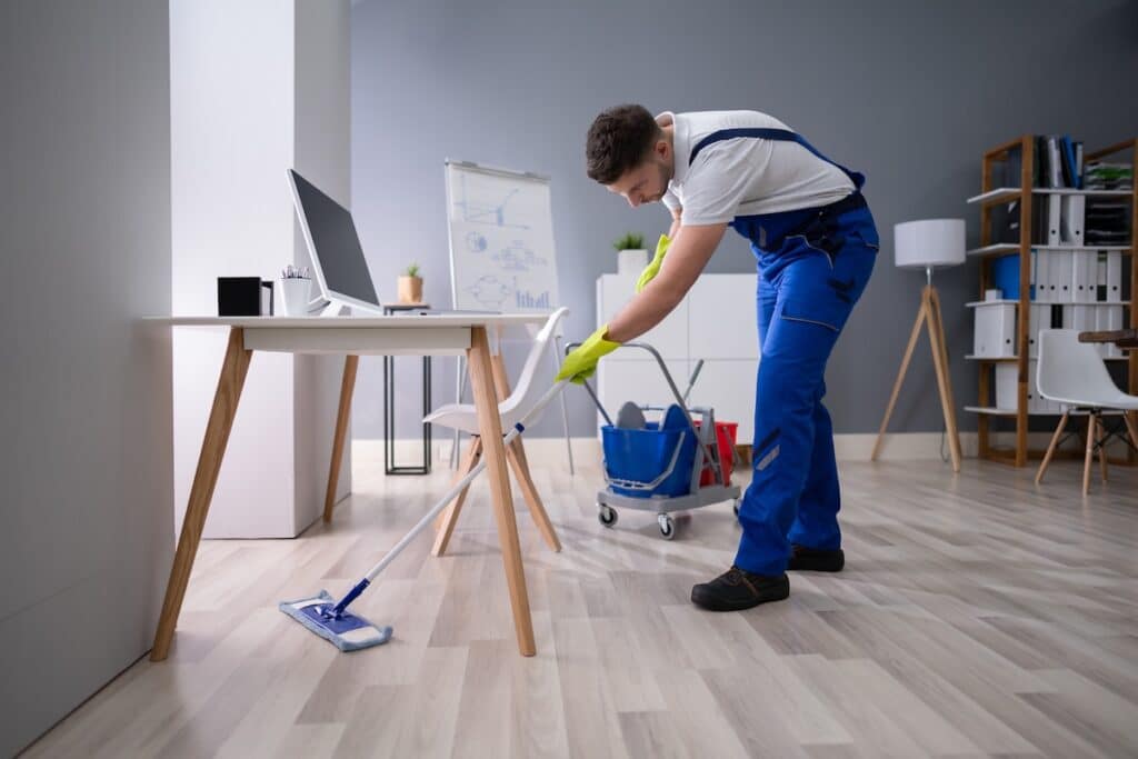 happy male janitor mopping floor in office