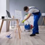 happy male janitor mopping floor in office